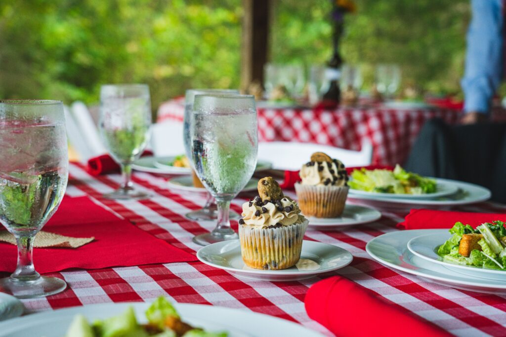 Table set for outdoor event with glasses of water, salads and a cupcake